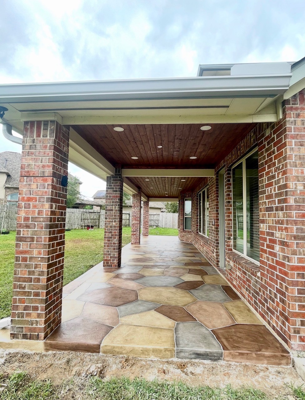 Covered patio with brick columns, wood ceiling and stained concrete floor by Art & Floors
